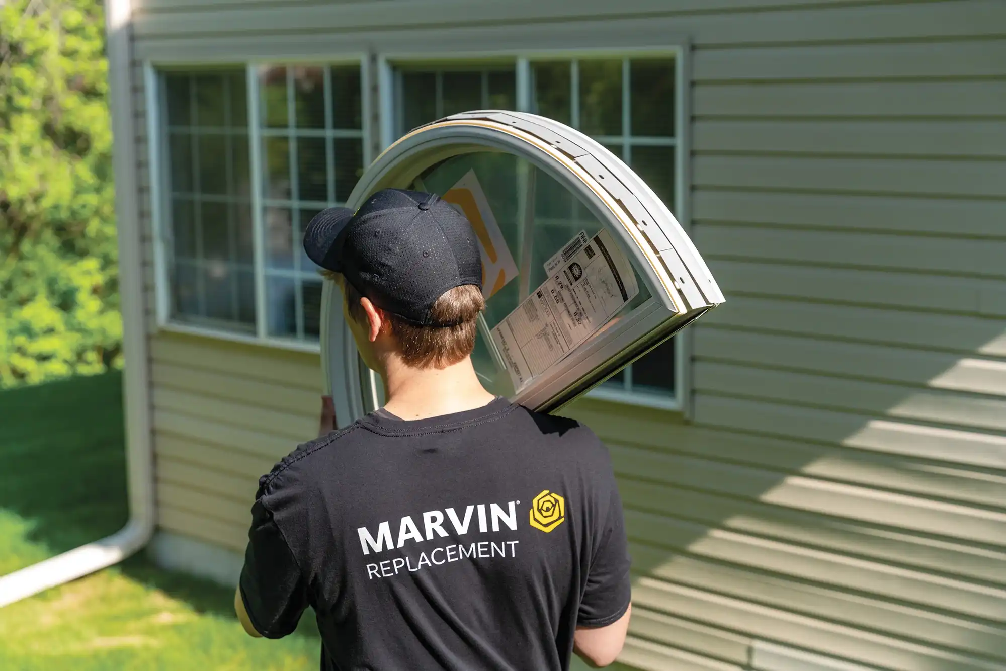 Marvin Replacement window installer in a black hat and black shirt carries a Round Top window.