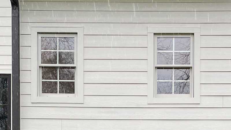 Exterior view of a home with white siding and white double hung windows next to each other.