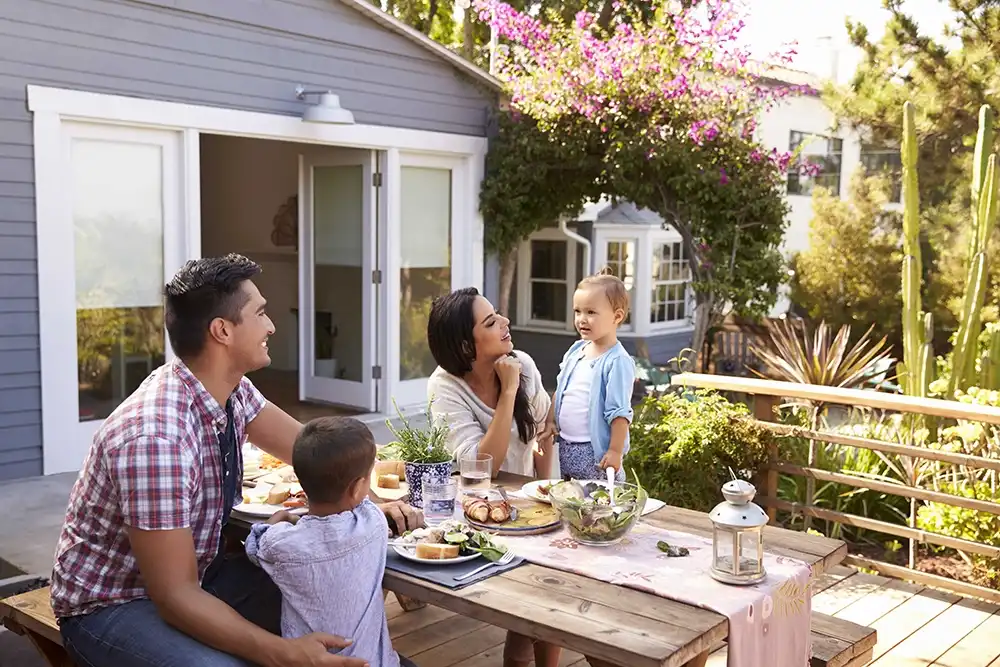 family on patio sitting at a wood picnic table filled with food