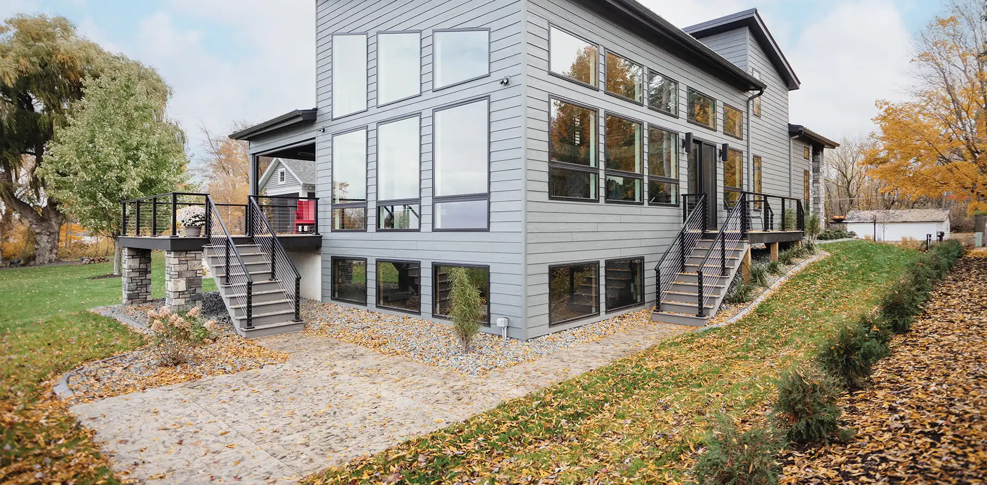 A gray home exterior in fall featuring black Marvin Replacement Picture, Awning and Special Shape Windows