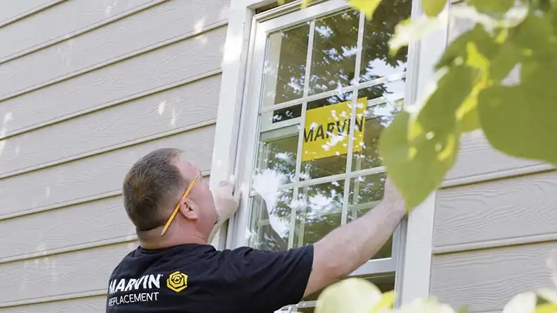 Marvin Replacement window installer places a white window into a window from the outside.