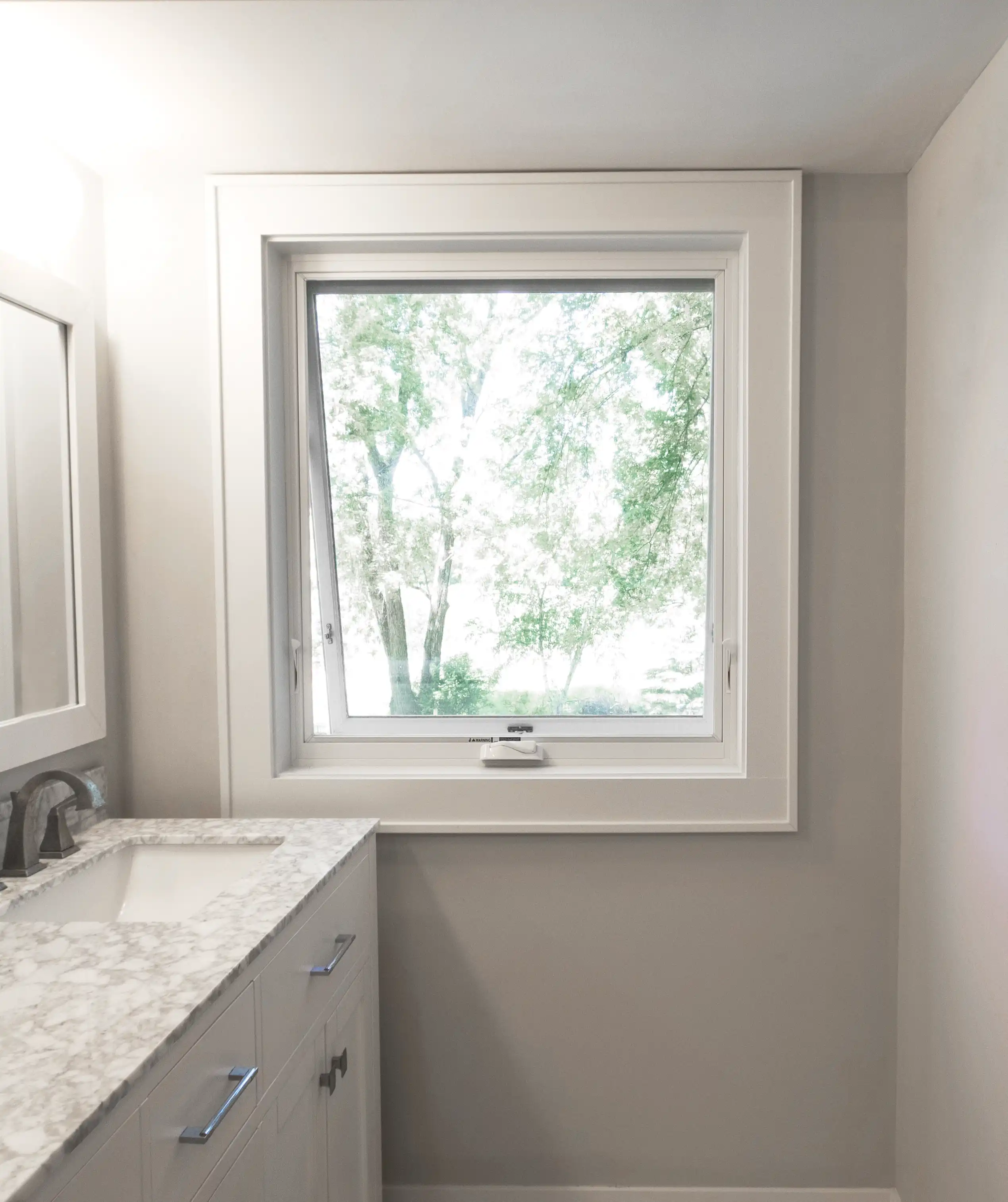 View of an open Marvin Replacement Awning window in a white bathroom with marble countertop.