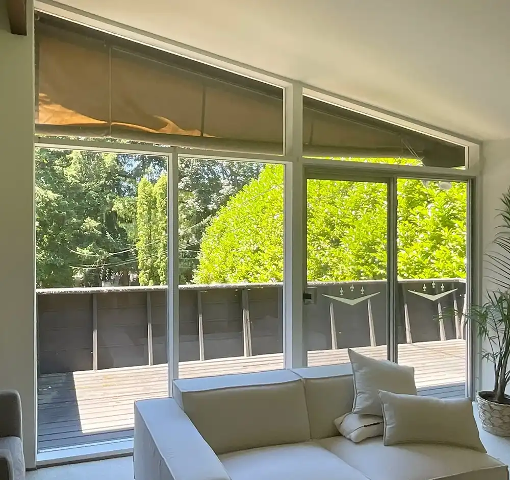 Interior view of old trapezoid picture windows in a living room with a view of a deck.