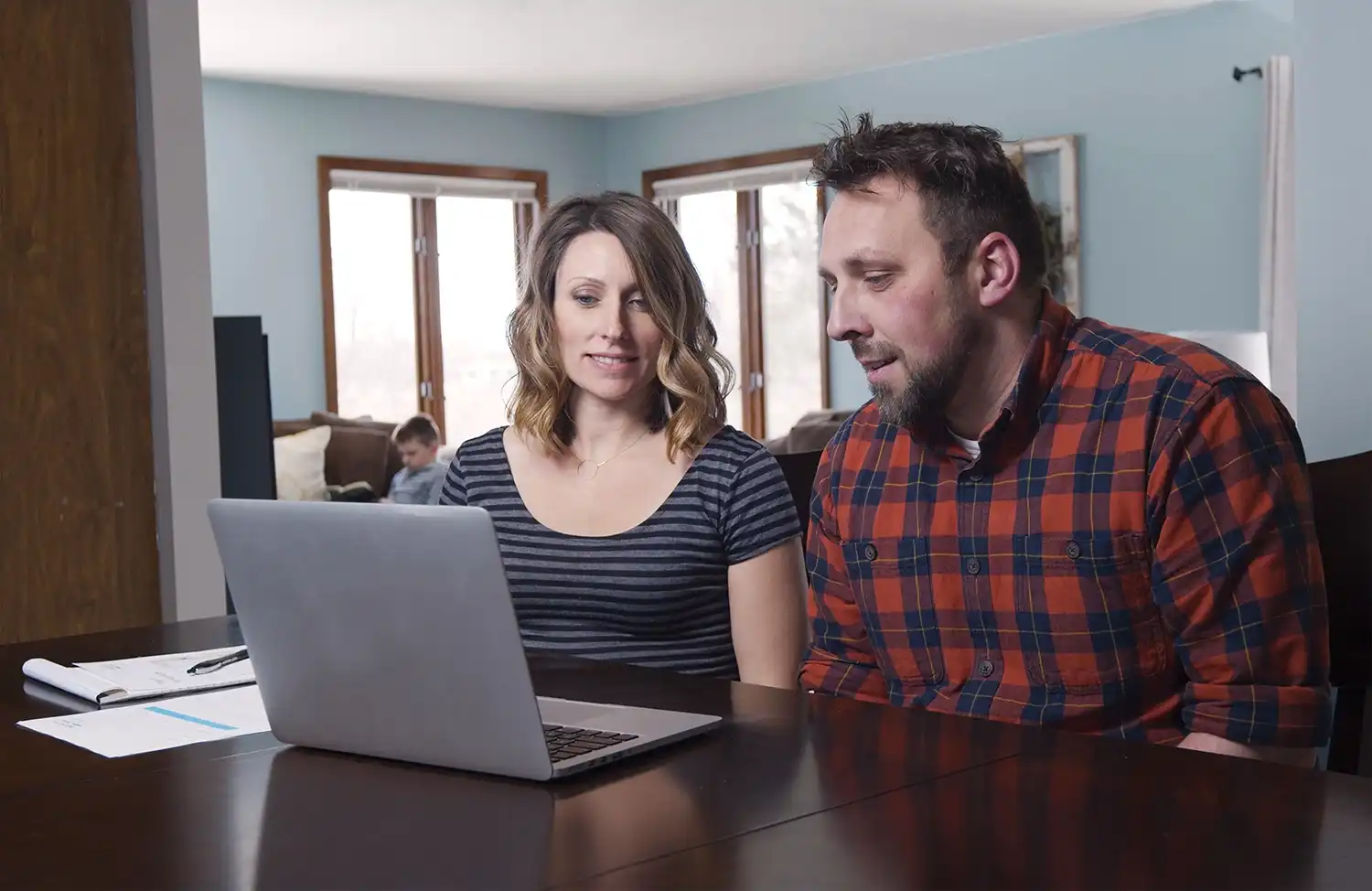 A man and a woman sit at a table and look at a laptop computer during a Marvin Replacement virtual consultation.