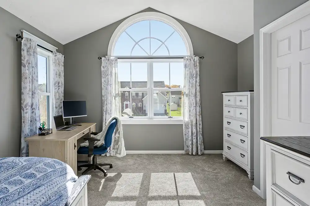 Interior view of a gray bedroom featuring an arch window above two double hung windows.