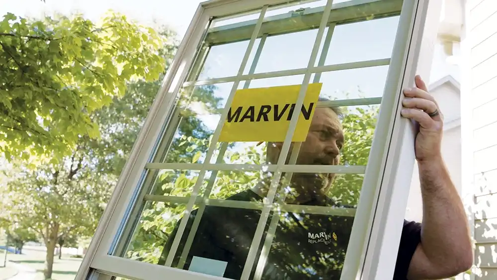 A man carries a white Marvin Replacement window with divided lites.