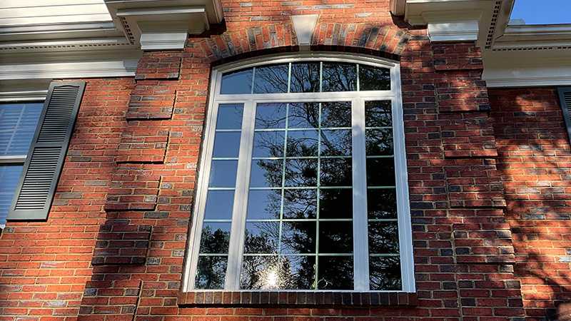 Exterior view of a Marvin Replacement Round Top window above a picture window with white divided lites on a brick home.