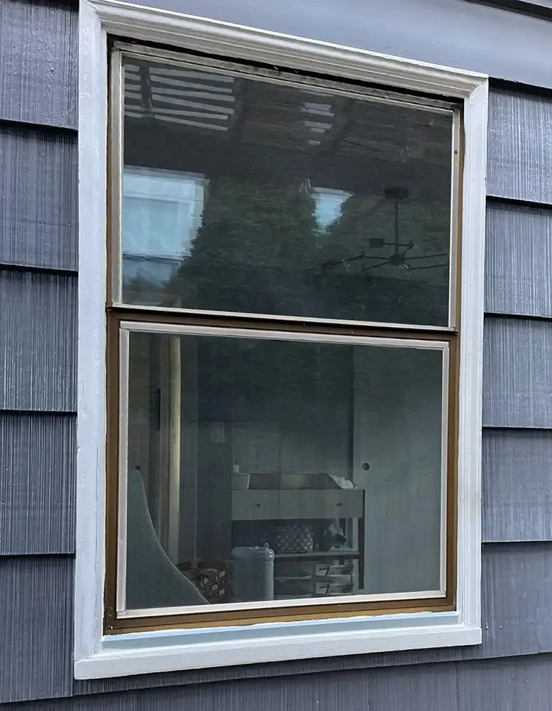 Exterior view of an old wooden double hung window on a blue house with white trim