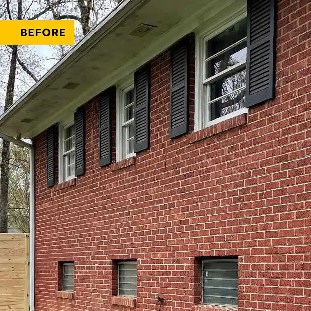 Exterior view of a brick home with old white windows and black shutters.