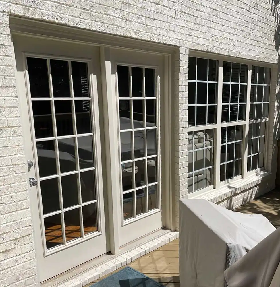 Exterior view of a two-panel French door next two three double hung windows on a patio.