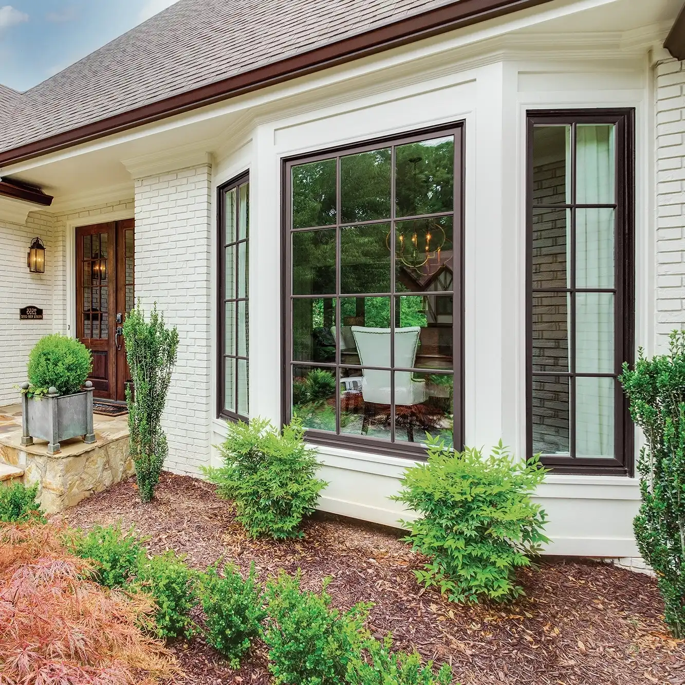 Exterior view of a white brick home featuring Marvin Replacement Casement windows and a picture window with grilles.