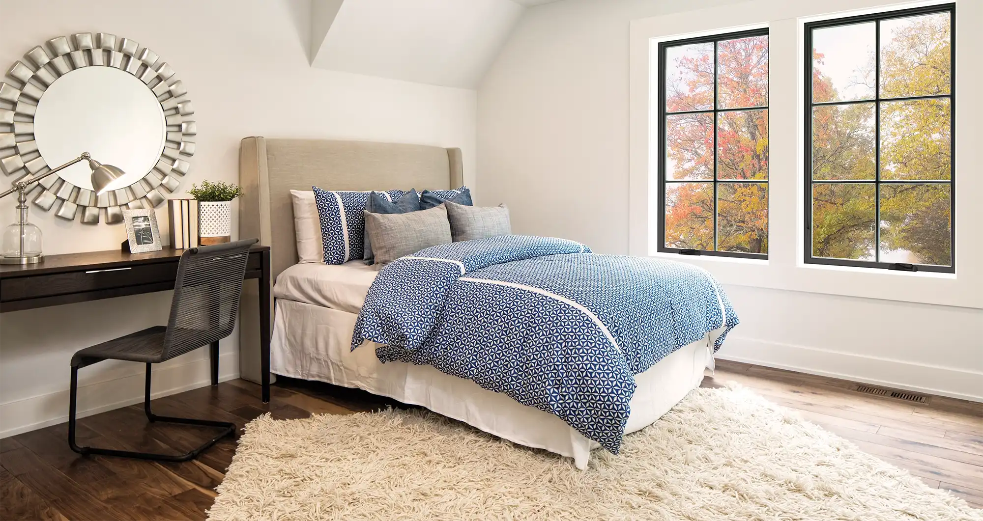 Interior view of a bedroom with black windows showing the changing colors of leaves outside.